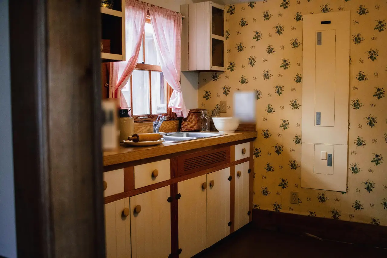 Avant : cuisine vieillie, papier peint à fleurs et armoires crème.